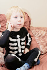 A child in a skeleton costume sits on the couch with an emotion on his face - 498675796