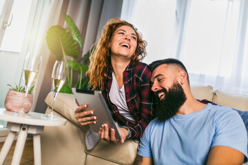 Young couple watching media content online in a tablet sitting on sofa in the living room