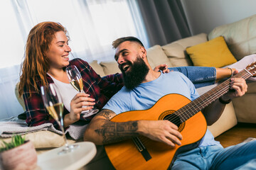 Couple is spending romantic moments together. The man is playing the guitar with his beloved...