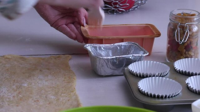A woman butters a rolled out dough. Prepares cruffin with raisins and candied fruit. Dishes and ingredients are laid out on the table.