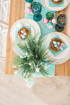 Easter pink and blue eggs on served table. Holiday spring composition with nest, glasses and plates