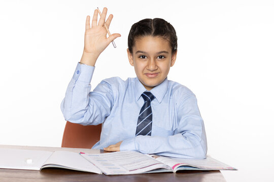 young girl of primary school sitting in classroom raising hand to respond to a question isolated on white background