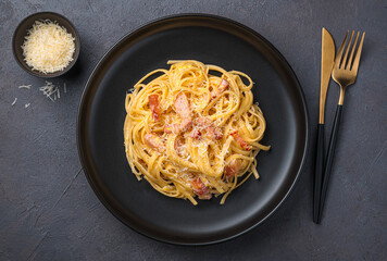 Linguini pasta with carbonara sauce on a dark plate.