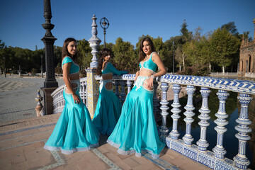 three belly dancers dressed in light blue leaning on the railing of a bridge. They are talking to each other and looking at the camera. Belly dance and Indian dance concept. Folklore