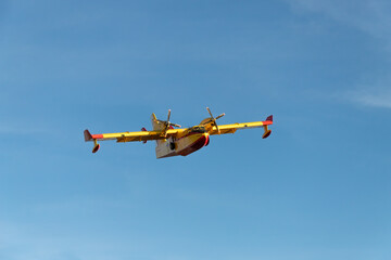 Hydroplane for the extinction of forest fires flying in a deep blue sky. Red and yellow aircraft. Front view. Isolated.