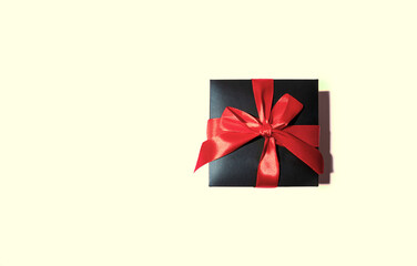 Black Gift box with red bow on beige background.. Top view and copy space.