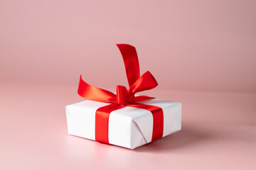 Gift box wrapped in white paper with red ribbon on pink  background. Gifting and surprise concept.
