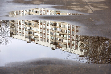 Puddle after rain with reflection of residential building in water. City street at rainy weather in spring