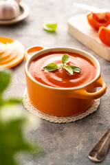 Tomato soup with fresh basil in orange bowl. Bright background. Healthy food concept.