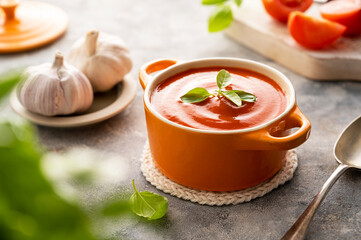 Tomato soup with fresh basil in orange bowl. Bright background. Healthy food concept.