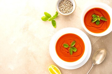 Tomato soup with fresh basil in white bowls. Bright background. Top view, copy space.