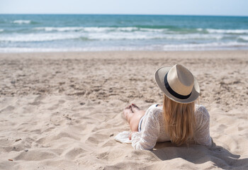 Young woman in white shirt and hat lies on back on sand beach and look far away. Vacation, travel and holiday on sea. rest on weekend. 