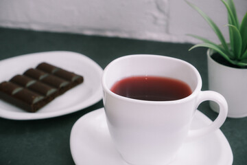 Sweet chocolate snack. White cup of tea close-up of a bar of chocolate in the background. World Chocolate Day and snack or breakfast concept.