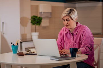 Fototapeta premium Woman working on a laptop in the kitchen at home