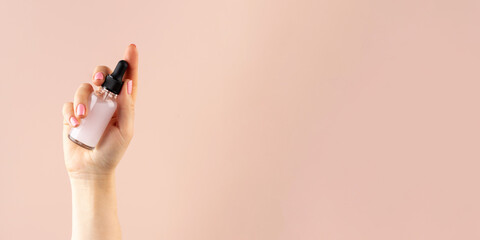  Mockup of a glass dropper with facial moisturizing oil in a female hand on a pink background. Copy space.