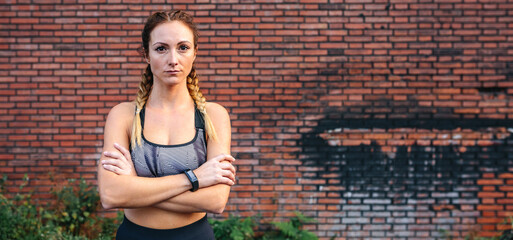 Sportswoman with crossed arms posing in front of a brick wall