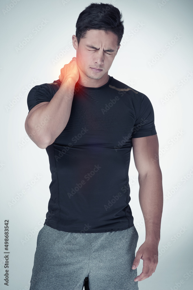 Wall mural Injuries can occur no matter how careful you are. Studio shot of an athletic young man suffering with neck pain against a grey background.