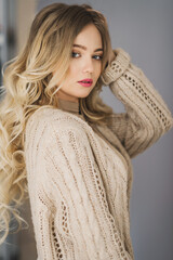 Young blonde curly woman in beige knitted cardigan portrait