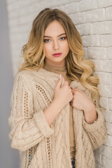 Young blonde curly woman in beige knitted cardigan portrait