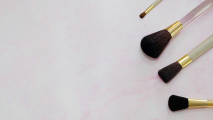 Flat lay of make-up brushes in different sizes. On a pink marble-like background.