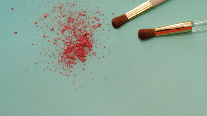 Closeup photo of the tip of two makeup brushes, with bits of red cosmetic blush powder near the brush tip.
