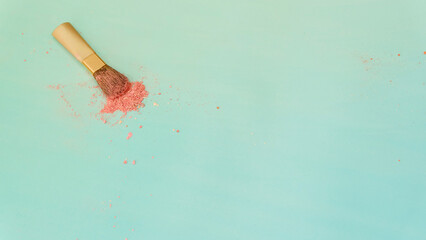 Top view of a small blush applicator brush, with a pile of pinkish makeup powder center around the brush head. On a bluish green background. With copy space on the right.