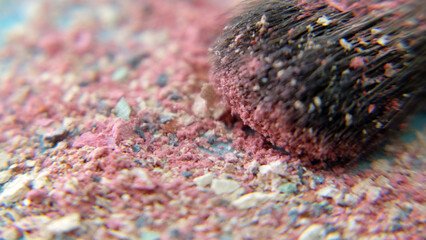 Closeup of the hair of brush head, covered with makeup powder, with a pile of colorful cosmetic powder bits under the brush.