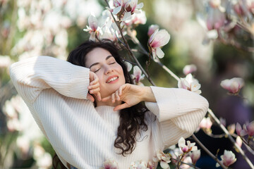 Beautiful girl with flowers of magnolia. Portrait of young smiling brunette woman under blossom magnolia tree. © Chernysheva