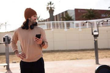 Young muscle man using the phone outside. Fit handsome man resting after training.