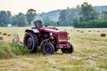 old red tractor in the field mows the grass