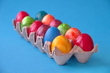 Colorful Easter eggs in cardboard box against blue background