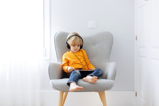 Barefoot boy in headphones watching cartoons on tablet
