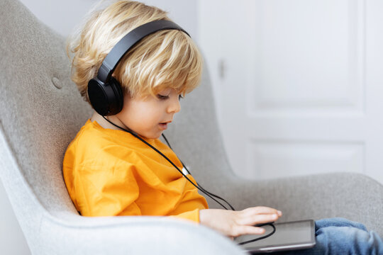 Side view of boy in headphones watching cartoons on tablet
