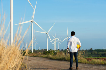 person with turbine in the field.Young  engineer working in wind turbine farm on blue sky background. Young  engineer working on substation and  wind turbine farm on blue sky background.