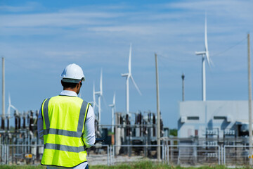 engineer at work. Young  engineer working in wind turbine farm on blue sky background. Young ...