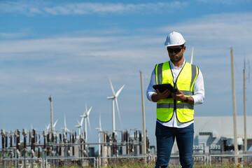 Young  engineer working in wind turbine farm on blue sky background. Young  engineer working on...