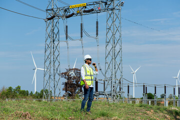 Young  engineer working on substation and  wind turbine farm on blue sky background.