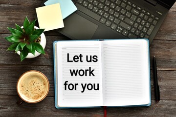 Notebook with the text LET US WORK FOR YOU near a laptop and green plant, pen, cup of coffee on a wooden background. Flat lay. Top view with copy space