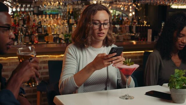 diverse group of friends having drinks in restaurant taking pictures of cocktails