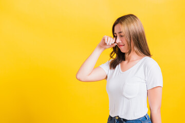 Asian Thai portrait beautiful cute young woman in depressed bad mood her cry wipe tears with fingers, studio shot isolated on yellow background with copy space
