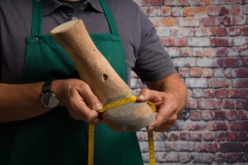 close-up of hands of orthopedic shoemaker controlling an individual wooden last to make an individual shoe with a measurement tape