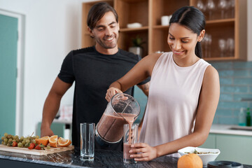 Can I pour you a glass. Cropped shot of an affectionate young couple making smoothies in their...