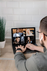 Back view of stylish male employee having an online conference with colleagues, using a laptop. Young businessman discussing corporate project with coworkers by video call, internet meeting concept