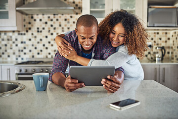 Check this out. Cropped shot of an affectionate young couple using a tablet in their kitchen at...