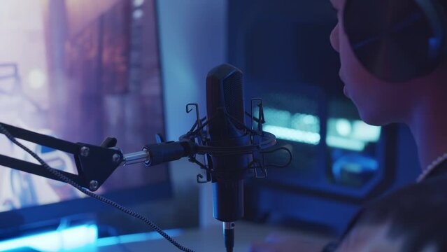 Slowmo of Biracial teenage boy in headphones speaking in microphone while playing first person shooter game on computer in dark roomSlowmo of Biracial teenage boy in headphones speaking in microphone 