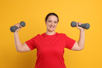 Fototapeta na wymiar Happy overweight woman doing exercise with dumbbells on orange background