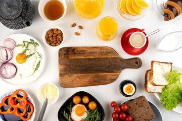 Delicious family breakfast table with coffee, tea, orange juice, croissants, toast, butter, fried and boiled eggs, avocado, cherry tomatoes, almond and salad. Copy space.