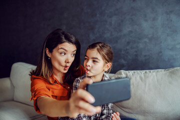 Mother and daughter taking selfie and making silly faces.  - obrazy, fototapety, plakaty