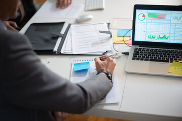 Back view of businessman analyzing graphs. Serious man working at table looking at computer writing down market data, making forecasts with team. Financial analytics and business activity concept