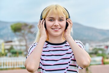 Outdoor portrait of a smiling young female teenager in headphones, looking at camera